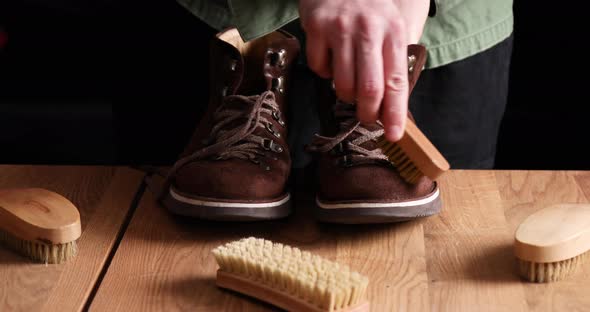 Man's hand clean suede shoes, boots with a brush on wooden background.