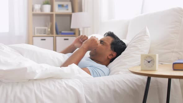 Indian Man in Bed Reaching for Alarm Clock