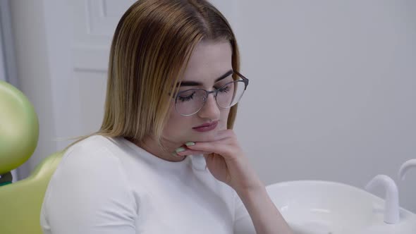 Sad Female Patient Sits on Dental Chair with Toothache and Waits for Theatment