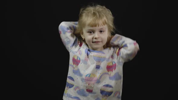 Little Baby Girl in Pajama Is Fooling Around and Make Faces. Black Background