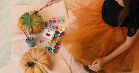 Little girl drawing face on orange Halloween pumpkin