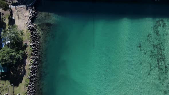 Moving drone view looking down at a clear water river close to a busy road and bridge leading to a p