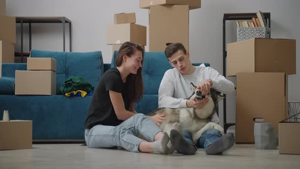A Lean Man and a Slender Girlfriend are Stroking Their Dog in a New Apartment
