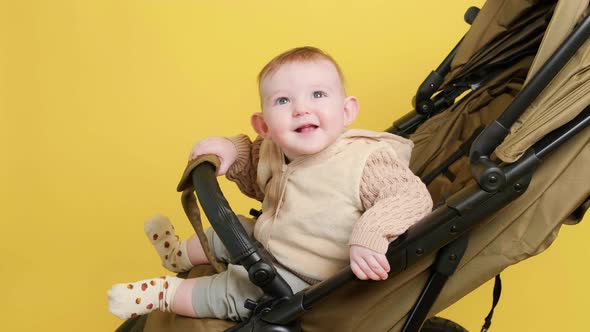 A happy child is sitting in a baby carriage on a studio yellow background. Smiling toddler baby boy