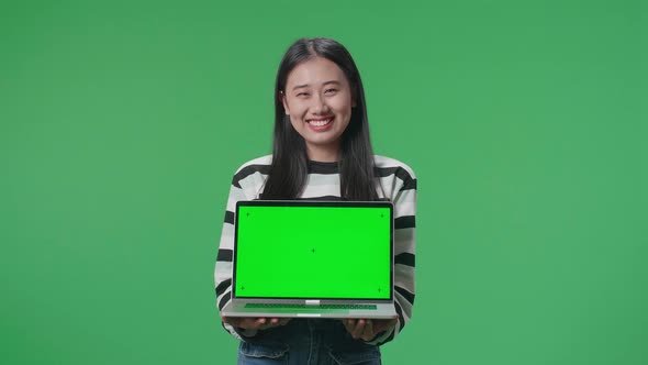 A Smiling Asian Woman Holding Green Screen Computer While Standing In Front Of Green Screen