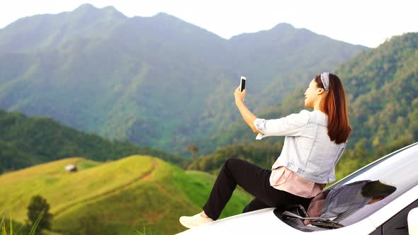 Young woman traveler sitting on a car watching a beautiful mountain