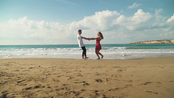 Young Man and Woman Spinning Around Holding Each Other Hands on the Beach. Cute Lovers Happy