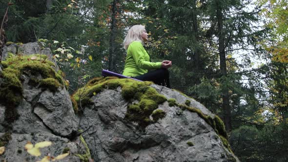 Woman meditating on a rock in the forest