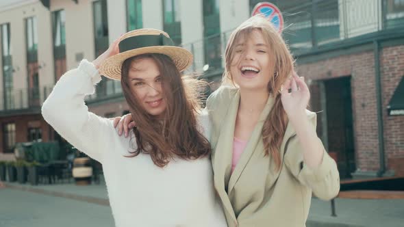 Two young beautiful smiling hipster girls in trendy clothes posing outdoors