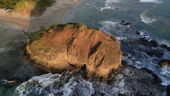 Drone slowly approaching a giant rock at playa grande in Tamarindo, Costa Rica. Few people walking a