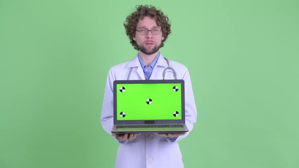 Happy Young Bearded Man Doctor Talking While Showing Laptop
