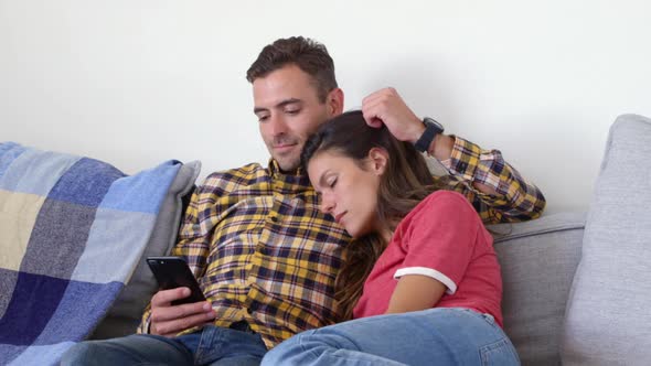 Cute man using mobile phone and woman relaxing on his shoulder in living room 4k