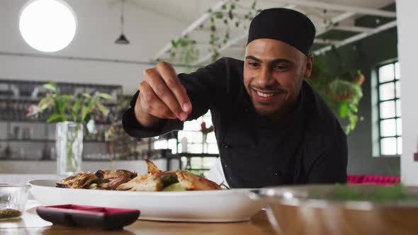 Mixed race male chef preparing a dish and smiling in a kitchen