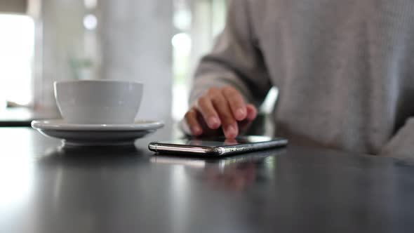 Closeup of a woman touching and scrolling on smart phone screen with coffee cup on the table