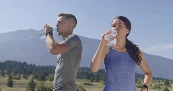 Slow Motion Shot of a Couple of Joggers Drinking Water Resting After Intense Training in Nature