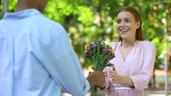 Mixed-Race Teen Boy Presenting Flowers to Surprised Girlfriend, Date in Park