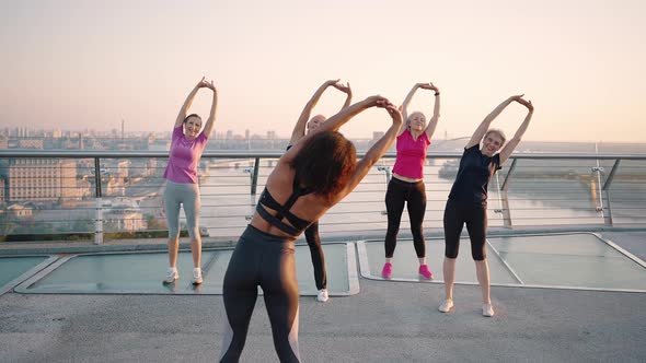 Group of Active Mature Ladies Warming Up with Sport Coach Training Together on Bridge Tracking Shot