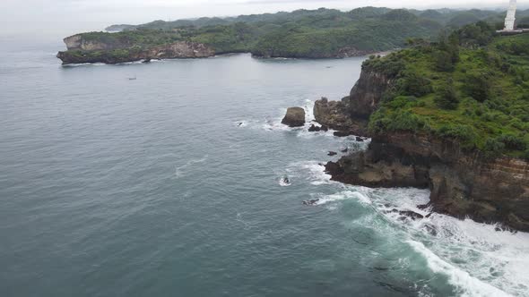 Aerial view of tropical beach in Gunung kidul, Indonesia with green and rocky cliff.