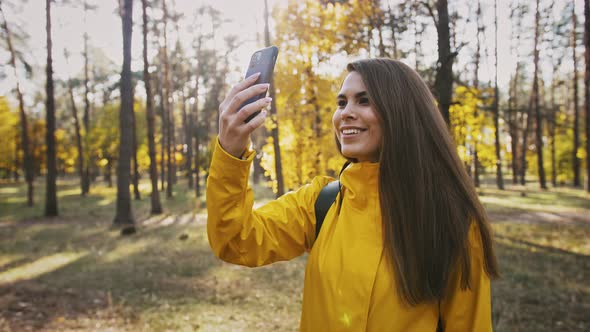 Young Woman Smiling Taking Photos of Environment and Selfies on Her Smartphone During Walk in Autumn