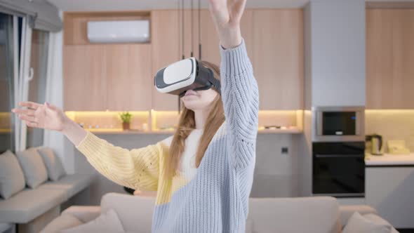 Young girl at home in virtual reality glasses plays, communicates, has fun. Uses in VR helmet at