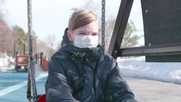 A Guy Is Sitting on a Swing in a Protective Mask on the Playground.Prevention and Protection of