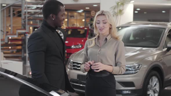 Pretty Caucasian Woman Giving Car Keys To the African American Man in Automobile Showroom