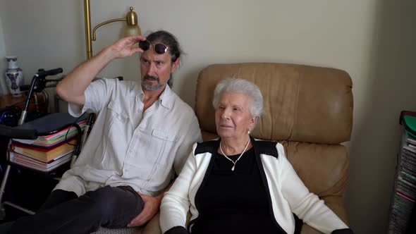 Elderly woman and mature son talk and discuss, both looking off camera.