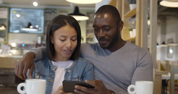 Happy Mixed Race Couple Using Mobile Phone While Drinking Coffee in Cafe