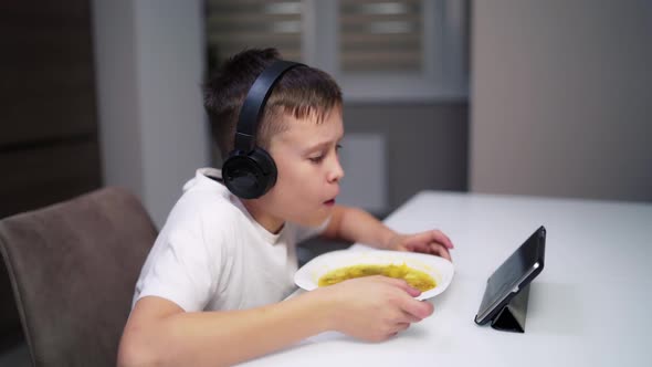 Boy eating at home while looking at digital tablet. 