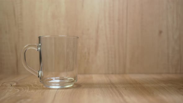 A man's hand uses a metal spoon to add tea to the cup. The background is made in woody texture