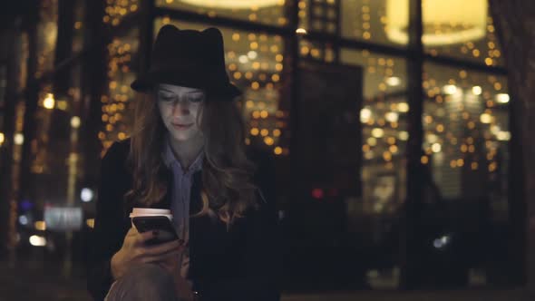 Young Woman In Night Town Using Mobile Phone And Walk Street