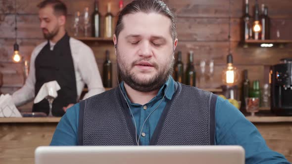 Young Businessman in a Small Coffee Shop Drinks Coffee During a Video Call