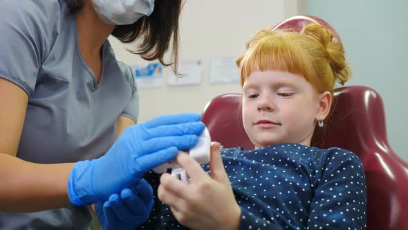 Dentist Showing Little Girl How To Clean the Teeth with Toothbrush Properly on Jaw Model at Dentists