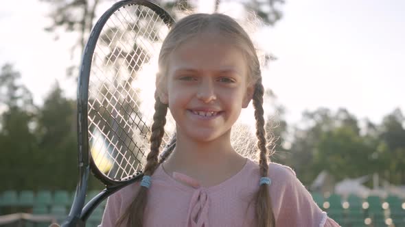 Portrait Cute Little Smiling Girl with Pigtails and a Tennis Racket on Her Shoulder