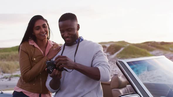 African american couple using digital camera to take pictures while standing near the convertible ca