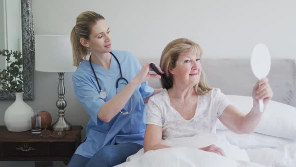 Female health worker brushing hair of senior woman at home