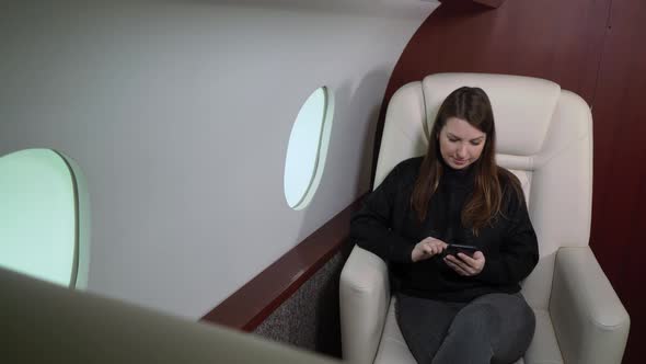 Woman in Airplane with Mobile Phone Using Smartphone in First Business Class or Private Jet Flight