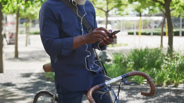 African american senior man using smartphone while sitting on bicycle on the road