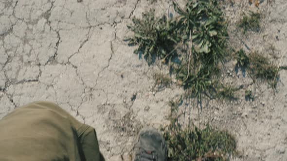 A Young Traveler Man in Green Pants and Black Boots Walks Through the Dry, Lifeless, Cracked Earth.
