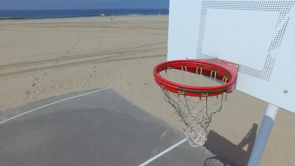 A man takes a jump shot while playing one-on-one basketball hoops on a beach court.