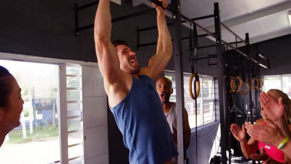 Men performing pull-up exercise while friends applauding him