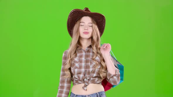 çGirl in a Hat and Cowboy Boots Comes with Bags in Her Hands. Green Screen