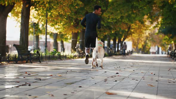 Young African American Black Man Running with His White Labrador Dog Through the Park in the City at