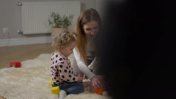 Happy Mother and Twin Daughters Playing Toys As Unrecognizable Person Passing at Front