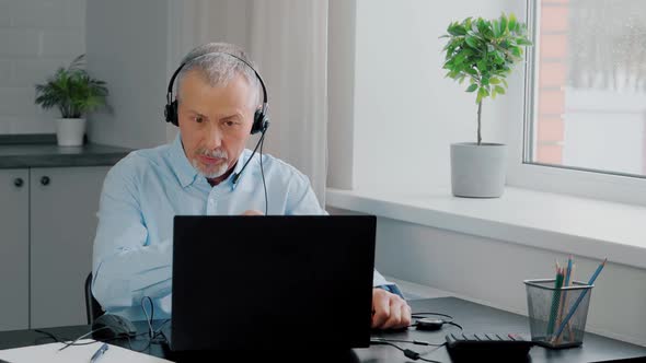 A Focused Businessman Wearing Headphones Takes Part in Online Negotiations