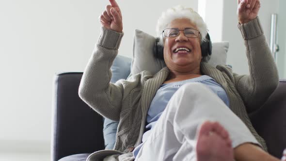 African american senior woman wearing headphones listening to music sitting on the couch at home