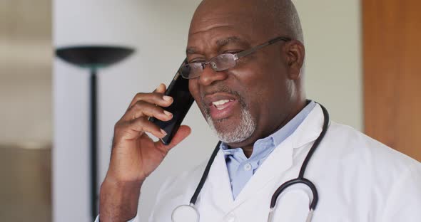African american senior male doctor wearing white coat talking on smartphone
