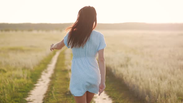 Woman in Beautiful Waving Dress Walks on the Meadow Happy Summer Vacation Sky at Sunset