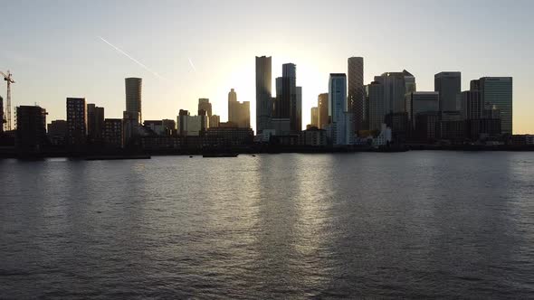 Aerial drone flight over River Thames showing silhouette of skyscraper buildings in Canary Wharf Dis