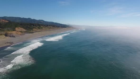 AERIAL: Traffic speeds by on a coastline highway as waves crash against the Oregon shore.